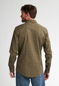 Camisa de manga larga en verde oliva con un sutil patrón geométrico, que presenta un cuello de punta y puños abotonados.