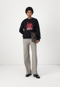 Sweatshirt preto com padrão de corações vermelhos e texto branco com a inscrição "Kool," combinado com calças cinza xadrez e segurando uma clutch castanha.