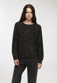 Czarny sweter dzianinowy z srebrnymi zabrudzeniami, okrągły dekolt i długie rękawy. Tkanina ma teksturowany wygląd i dopasowane mankiety.