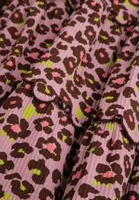 Sukienka warstwowa w różowym materiale z brązowymi plamkami pantery, zielonymi akcentami i różowymi detalami; wykończona falbaniastym dołem.