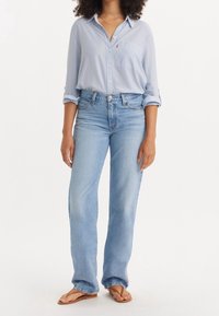 Camisa de botones a rayas de color azul claro con un bolsillo en el pecho, combinada con unos vaqueros rectos de color azul claro y chanclas de color marrón claro.