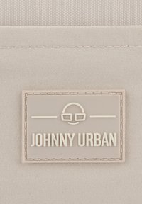 Tessuto beige chiaro con un motivo testurizzato, dotato di un'etichetta rettangolare in rilievo di colore crema che recita "JOHNNY URBAN" e un logo.