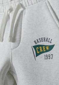 Graue Sweatpants aus weichem Stoff, mit einem Kordelzugbund und einem grün-gelben Grafikdesign mit dem Text "BASEBALL CREW 1997".