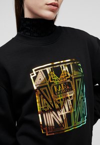 Felpa nera con collo alto, caratterizzata da un design geometrico lucido e multicolore e un logo al centro. Tessuto morbido con dettagli testurizzati.
