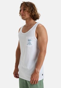 Camiseta de algodón blanca sin mangas con un bolsillo en el pecho que presenta un logotipo de palmera azul. Ajuste slim y cuello redondo, diseño sencillo sin patrones.