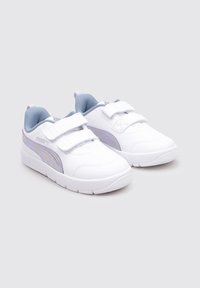 Sneakers bianchi per bambini Puma con accenti di viola chiaro e doppie fibbie in velcro su uno sfondo grigio.