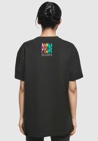 Svart t-skjorte med korte ermer med flerfarget «PRIDE SCOOPS»-tekst på baksiden. Klassisk passform med glatt tekstur og rund hals.