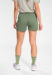 Gröna sportshorts med elastiskt midjeband, i kombination med matchande gröna mönstrade strumpor och vita löparskor. Slät tygtextur.