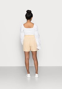 Bílý top s nadýchanými rukávy a nařaseným živůtkem v kombinaci se žlutými a bílými kostkovanými šortkami. Outfit doplňují bílé tenisky. Pohled zezadu.