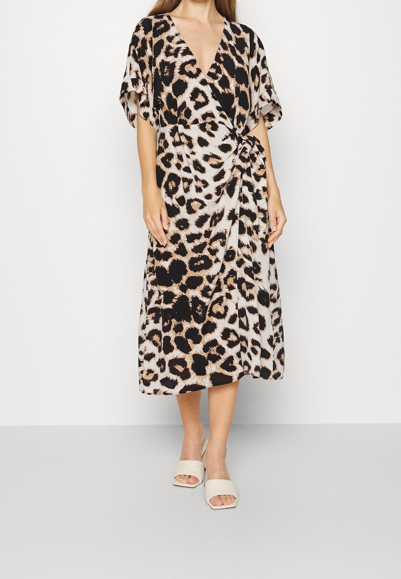 Slå-om-kjole med leopardprint, korte ærmer, V-udskæring og bindebånd i taljen. Flydende stof i beige, sort og tan nuancer.