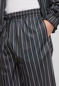 Pantalons de jogging rayés noir et blanc avec une taille élastique, des poches latérales et une texture de tissu lisse et léger.