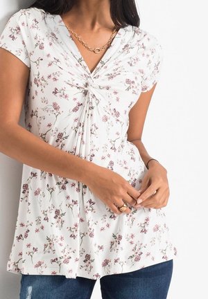 Top bianco a maniche corte con motivo floreale, caratterizzato da un design anteriore intrecciato con tonalità di viola e verde, realizzato in tessuto morbido e leggero.