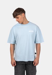 Světle modré bavlněné tričko s krátkými rukávy a kulatým výstřihem, na přední straně je bílým písmem vytištěno slovo "CRYSTAL".