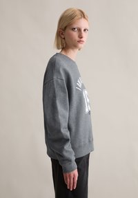 Szary sweter z miękkiego, teksturowanego materiału, z okrągłym dekoltem i nadrukowaną grafiką na klatce piersiowej. Długie rękawy z ściągaczami.