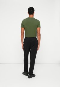 Grønn t-skjorte med korte ermer, svarte joggebukser og svarte sko. Enkelt design, myk tekstur og elastisk midje. Sett fra baksiden.