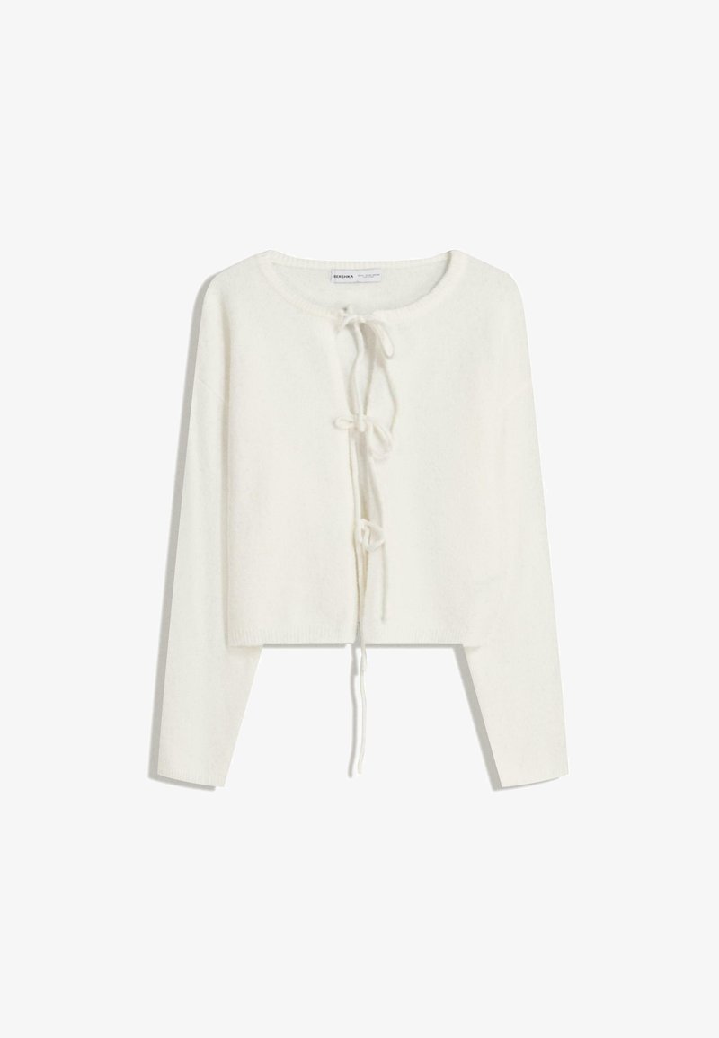 Gilet court à manches longues blanc avec col rond et trois fermetures à nouer à l'avant, en tissu tricoté doux.