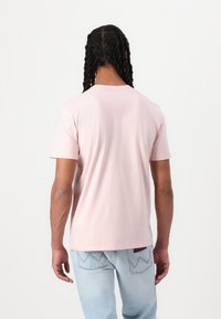 Rosa Baumwoll-T-Shirt mit kurzen Ärmeln und Rundhalsausschnitt. Hat eine glatte Textur und einen lockeren Schnitt, von hinten gezeigt. Helle Jeans.
