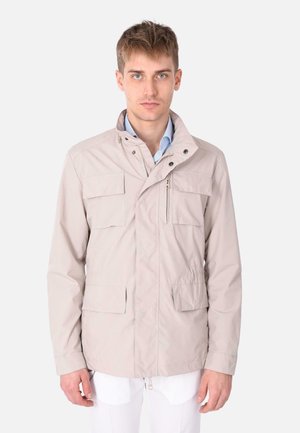 Giacca beige chiaro realizzata in tessuto liscio, con chiusura a zip, colletto alto e numerose tasche frontali per funzionalità.