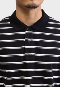 Polo de rayas blanco y negro con cuello, tapeta de tres botones y suave textura de tela.