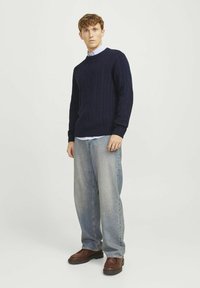 Navy knitted sweater with cable pattern, round neck, ribbed cuffs, paired with loose light blue jeans and brown leather shoes.