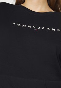 Musta puuvillainen t-paita, jossa on valkoinen "TOMMYJEANS" brodeerattu teksti ja pieni punavalkoisen ja sinisen logon yksityiskohta. Yksinkertainen pyöreä kaulus.
