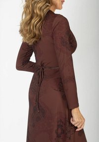 Brązowa sukienka z długim rękawem, zdobiona misternym ciemnym wzorem paisley, z talią wszytą w sznur i gładkiego, elastycznego materiału.