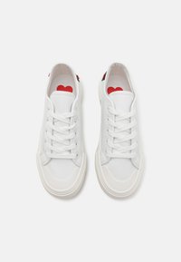 Sneakers bianchi con tomaia in pelle liscia, lacci bianchi piatti e suola in gomma. L'interno presenta una grafica di un cuore rosso sulla soletta.