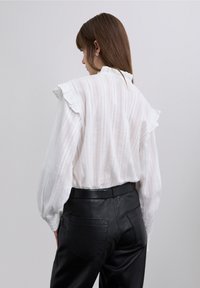Witte blouse met lange mouwen en gerimpelde schouders, met een gestructureerd oppervlak, gecombineerd met nauwsluitende zwarte leren broek met een gladde afwerking.