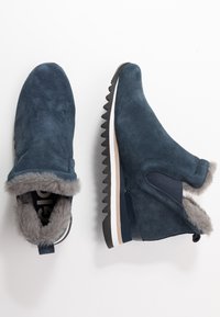 Bottines en suedine bleu marine avec doublure en fausse fourrure, panneaux latéraux élastiques et semelles en caoutchouc zigzag. Comprend une languette pour un enfilage facile.