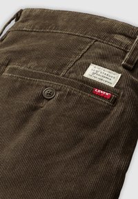 Brown corduroy pants featuring a back pocket with a Levi's label and a small red tag, with a textured, ribbed surface.