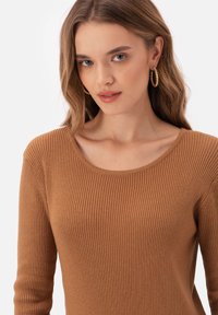 Brązowa, prążkowana bluzka z długim rękawem i okrągłym dekoltem. Miękka faktura, dopasowany krój oraz subtelne detale szwowe podkreślające projekt.