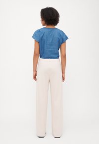 Top cropped de ganga azul com mangas curtas, combinado com calças largas à cintura de cor creme. Textura suave, detalhes mínimos, linhas limpas.