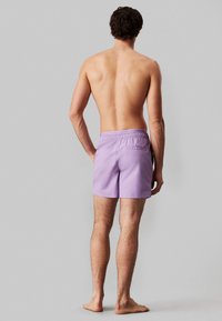 Pantaloni da bagno viola con vita elastica, texture sottile e tasca posteriori; lunghezza a metà coscia; senza motivi visibili o dettagli.