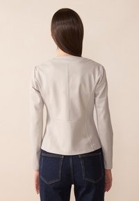 Grå kunstlederjakke med lange ermer, tettsittende design, sømdetaljer og avrundet halslinje, kombinert med mørkeblå denim jeans.