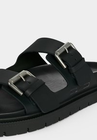 Μαύρο σανδάλι με ανοιχτά δάχτυλα, δύο ρυθμιζόμενες ασημένιες μεταλλικές αγκράφες και υφή στη σόλα.