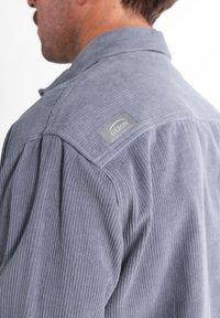 Camisa de pana gris con una superficie texturizada, que presenta un collar y un parche del logo Oxbow en el hombro.