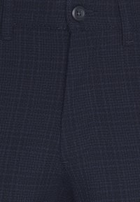 Tmavě modré strukturované kalhoty s jemným mřížkovým vzorem, zakončené jedním černým knoflíkem v pase a standardními kapsami.