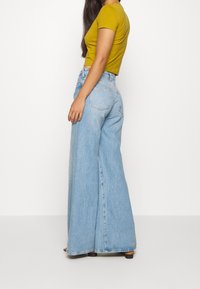 Lichtblauwe wijde jeans van denim met een hoge taille en twee achterzakken, gecombineerd met een mosterdkleurig, nauwsluitend, kortarmig shirt.