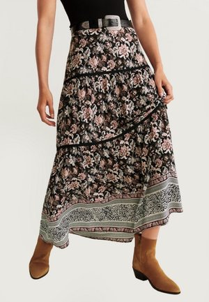 Jupe longue fleurie noire aux fleurs roses et blanches. Présente un design superposé et un ourlet à motif contrasté. Portée avec des bottines marron.