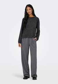 Camisola cinzento carvão com ajuste descontraído e mangas compridas, combinada com calças plissadas de cintura alta num cinzento mais claro. Sapatos pretos.