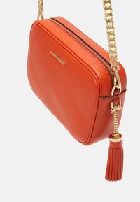 Pomarańczowa skórzana torebka na ramię z złotymi elementami, zamek błyskawiczny i akcent w postaci chwosta. Posiada teksturowaną powierzchnię i wytłoczone logo.