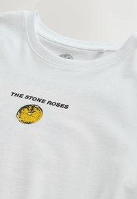 Valkoinen puuvillapaita, jossa on pyöreä kaula-aukko. Paidassa on musta teksti "THE STONE ROSES" ja keltainen pyöreä kuvio. Pehmeä rakenne.