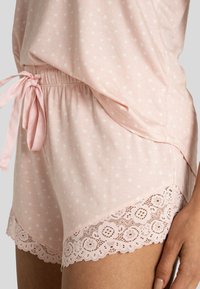 Rosa bomullsnattshorts med vitt stjärnmönster, elastisk midja med knytband och spetskant längs fållen. Mjuk textur och avslappnad design.