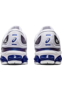 Scarpe sportive bianche con accenti blu, dotate di una parte superiore in mesh traspirante, suola spessa blu e un design distintivo con motivo a onde sul tallone.