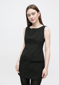 Vestido preto sem mangas feito de tecido liso com corte ajustado, apresentando um laço na cintura e um detalhe de racha na bainha.