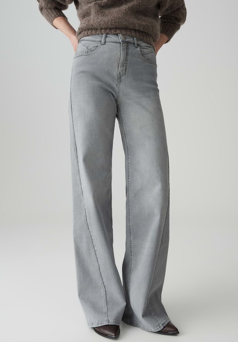 Jeans a gamba larga grigio chiaro con chiusura a bottone classica, tasche frontali e trama di denim liscia. Adatti in vita, larghi sulle gambe.