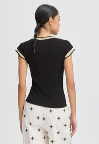 Top scurt, negru, cu guler ribbed și margini contrastante de o nuanță deschisă. Materialul pare neted și se potrivește bine la talie.