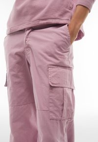 Pantaloni cargo rosa chiaro realizzati in morbido cotone. Caratteristiche includono tasche laterali e dettagli cuciti. Vestibilità casual con una silhouette leggermente ampia.