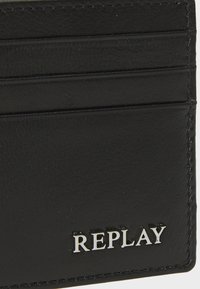 Černý kožený držák na karty s více sloty, s embosovaným logem "REPLAY" ve stříbrné barvě, viditelné švy na okrajích. Plochý, obdélníkový tvar.