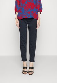 Marina smala byxor med uppvikta fållar, i kombination med svarta sandaler med breda remmar. Överdel med ett mönster av röda och blå blommor.